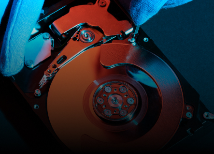 Close-up view of a person wearing blue gloves using a screwdriver to work on an opened hard disk drive in their home.