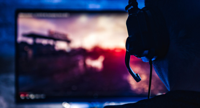 Person wearing a headset, viewed from behind, playing a video game on a screen with a blurred, colorful background that resembles federal insignias.