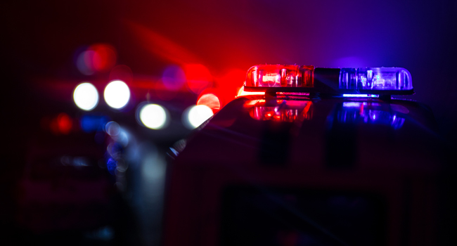 Close-up of a police car's flashing lights, with blurred red and blue lights in the background indicating other emergency vehicles in a dark setting, showcasing State & Local Technology Solutions at work.