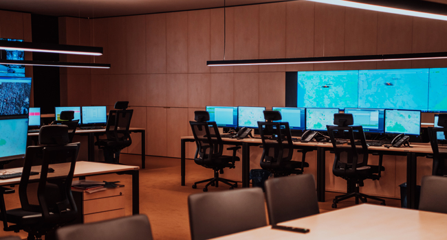 Several workstations with multiple monitors and telephones in a modern command center, showcasing advanced technology services, but no operators are present.