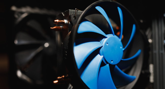 Close-up of a computer cooling fan with blue blades, attached to the heatsink and copper heat pipes, part of the internal hardware intended for cooling the computer components by New Technology Solutions.