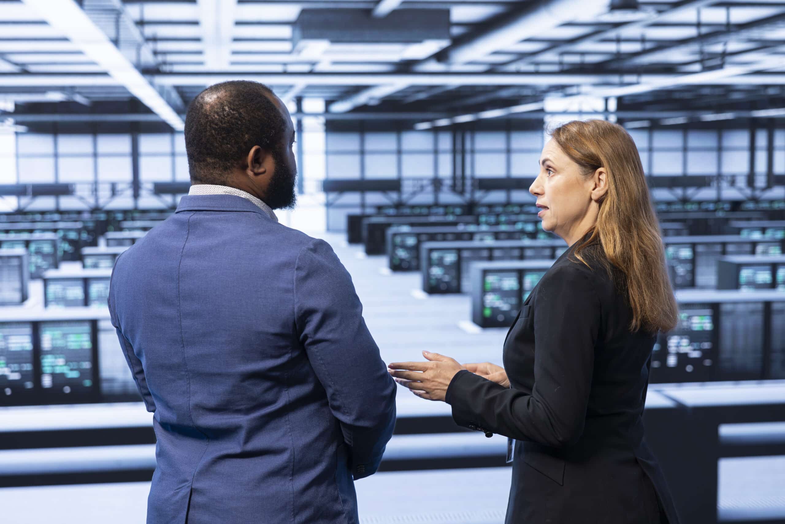 Two professionals in business attire stand in front of a large room filled with rows of computer servers, engaged in conversation about the Corvid HPC partnership.
