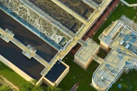 Aerial view of a wastewater treatment plant showcasing processing tanks, walkways, and adjacent buildings surrounded by grass, highlighting AI Sustainability efforts in modern infrastructure.