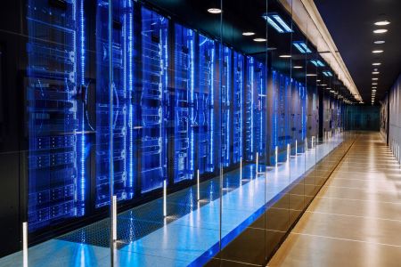 A modern server room with rows of illuminated blue server racks behind glass walls and a reflective floor, showcasing a high-tech environment designed with AI sustainability and EPEAT Climate+ standards in mind.