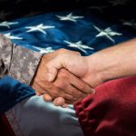 A person in military uniform shakes hands with a civilian, with a United States flag in the background, commemorating the signing of the $5 billion ADMC-3 Army contract.