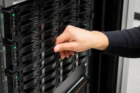 A person’s hand is inserting or removing a hard drive from a RAID server rack in a data center.