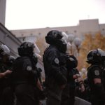 Group of law enforcement officers in helmets and protective gear assembled outside a building, facing various directions.