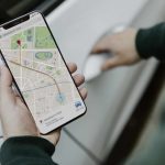 Person holding a smartphone displaying a map navigation app with directions to Madison Park, while opening a car door—perfect for demonstrating smartphone forensic search in real-world scenarios.