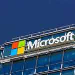 A modern office building with the Microsoft logo on the facade, featuring blue-tinted windows against a clear blue sky, stands as a reseller hub for tech enthusiasts and businesses looking to explore the latest Microsoft Surface innovations.
