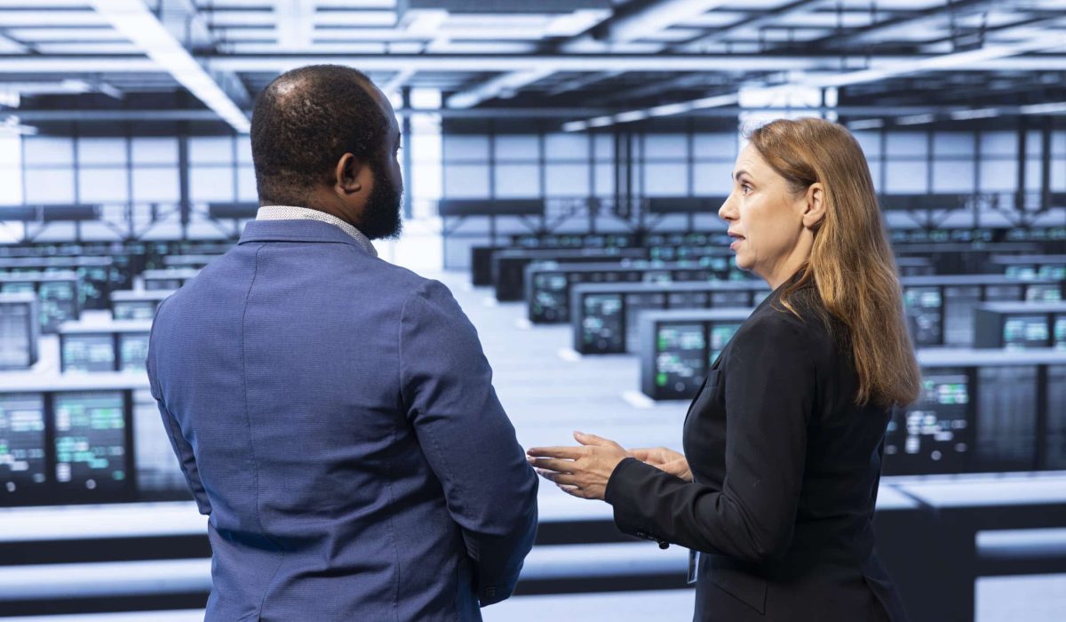 Two professionals in business attire stand in front of a large room filled with rows of computer servers, engaged in conversation about the Corvid HPC partnership.