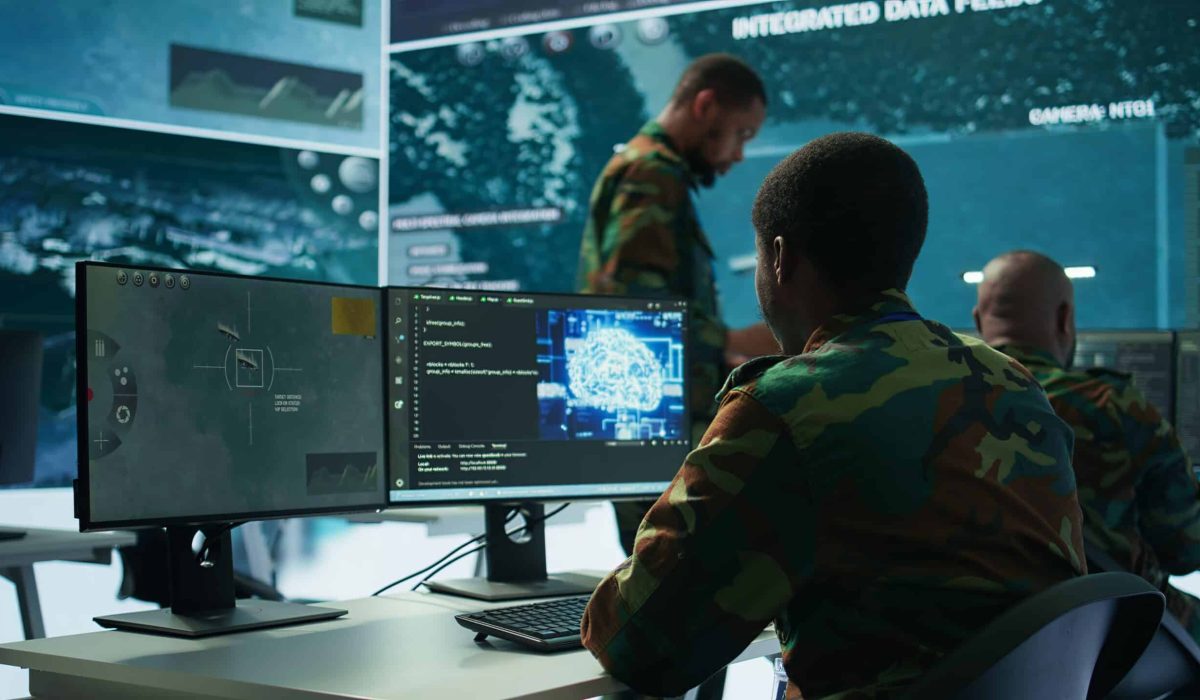 Military personnel in camouflage uniforms work at computer stations displaying surveillance data and maps, utilizing advanced Army Solutions in a high-tech operations room.