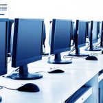 A row of idle high-performance workstations with monitors, keyboards, and mice in a bright, empty office or computer lab environment.